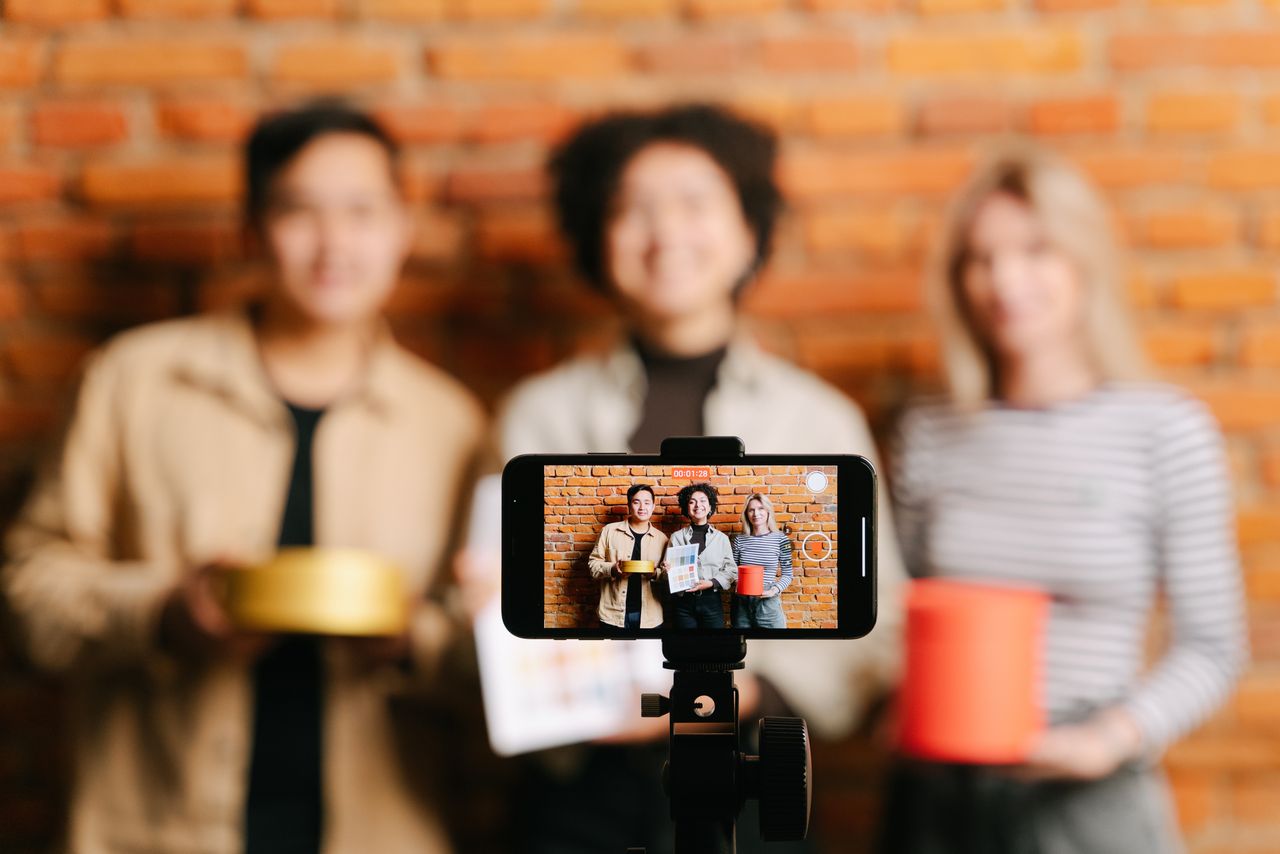 services-03 A diverse team of vloggers recording a video with a smartphone against a brick wall backdrop.